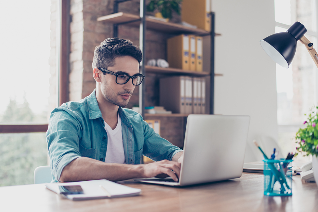 Man wearing glasses typing on his laptop